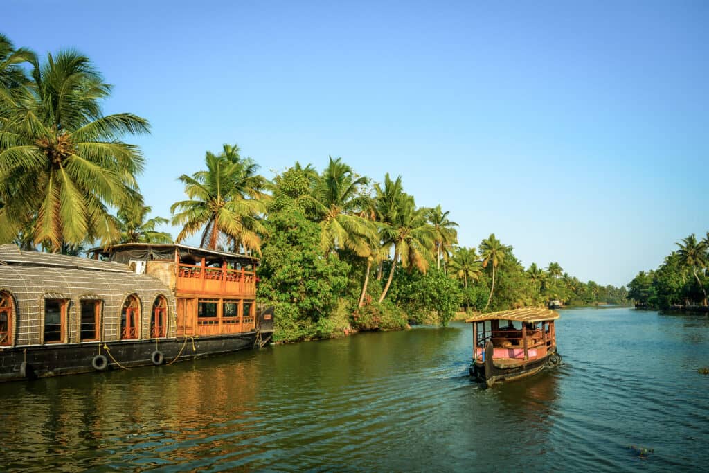 A tourist boat passes through a traditional Kerala houseboat on the backwater of Vembanad Lake