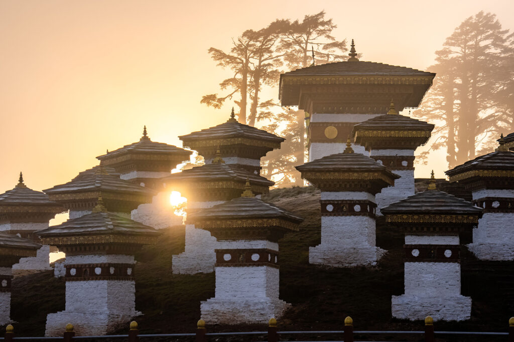 The sunrise through fog at the Dochula Pass Tibetan Buddhist Stupas Chorten in the Himalayas of Bhutan